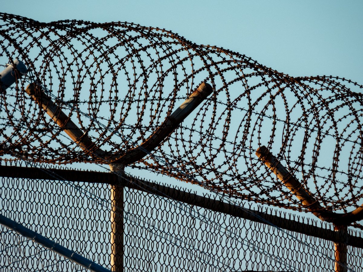 A mesh wire fence topped with razor wire and barbed wire on the perimeter