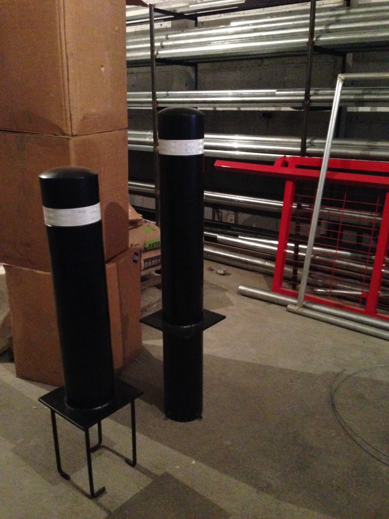 Two black bollard posts with white bands stand in an industrial garage setting near red safety gates and metal shelving.