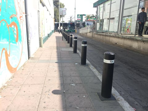 Urban street with bollards lining sidewalk, colorful graffiti on left wall, and storefronts on right