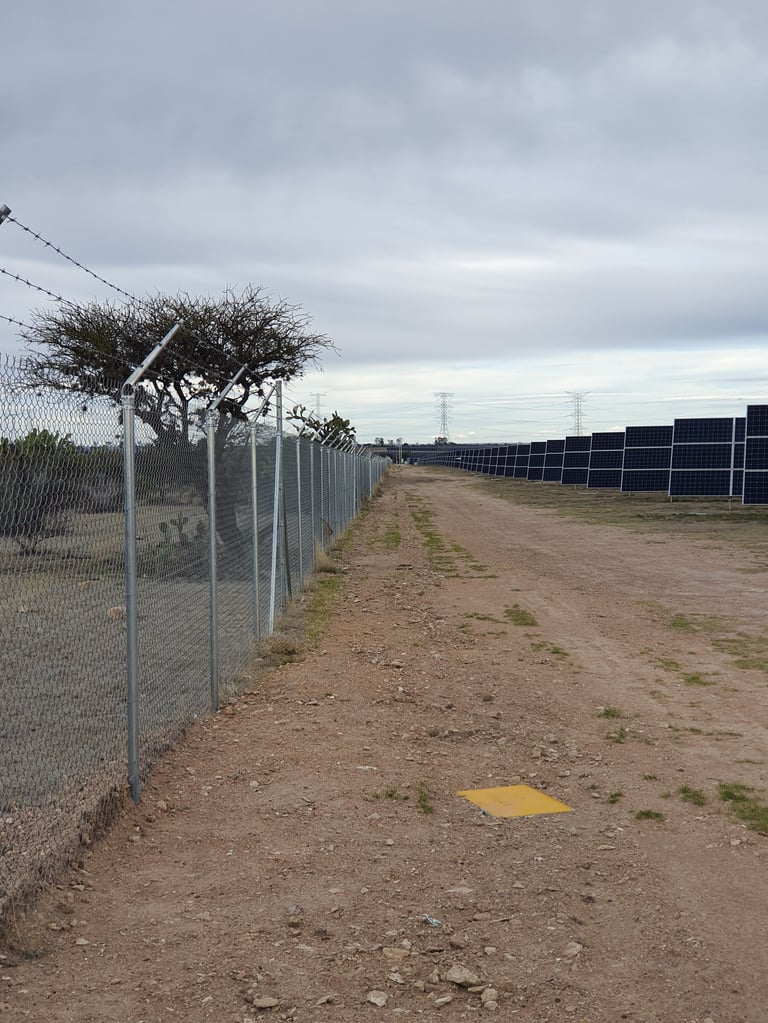 Carretera con cerca de malla ciclónica y paneles solares en parque fotovoltaico