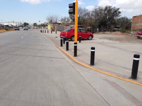 Red car parked at traffic light with yellow post and black bollards on paved street with bare trees